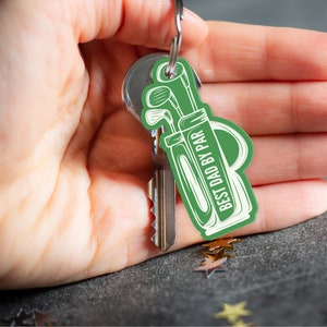 May include: Green golf bag keychain with the text "Best Dad By Par" in white. The keychain is attached to a silver key ring.
