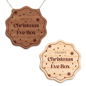 May include: Two wooden Christmas Eve boxes with a snowflake design. The top box is brown and says "MADDY'S Christmas Eve Box". The bottom box is light wood and says "OSCAR'S Christmas Eve Box".
