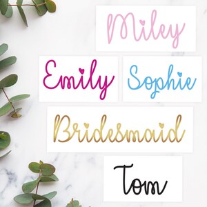 May include: Five white cards with different names written in colorful script. The names are Miley, Emily, Sophie, Bridesmaid, and Tom. Each name has a small heart symbol next to it.