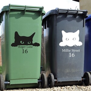 Puede incluir: Dos contenedores de basura con ruedas, uno verde y otro gris oscuro, con calcoman&iacute;as de caras de gato. El contenedor verde tiene una calcoman&iacute;a de gato negro con el texto "Roger Lane 16". El contenedor gris tiene una calcoman&iacute;a de gato blanco con el texto "Millie Street 16".