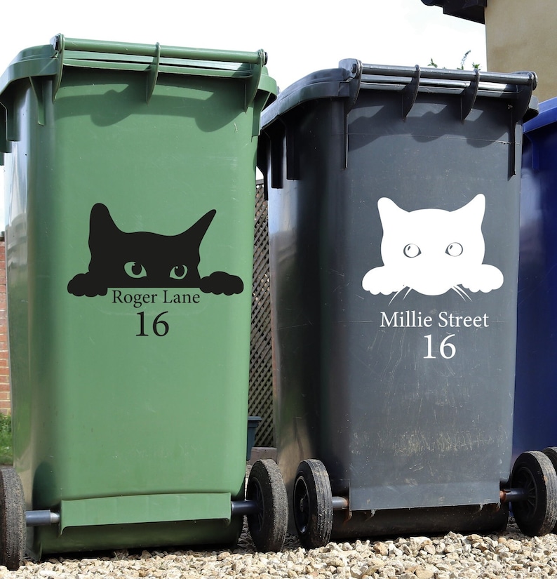 Puede incluir: Dos contenedores de basura con ruedas, uno verde y otro gris oscuro, con calcoman&iacute;as de caras de gato. El contenedor verde tiene una calcoman&iacute;a de gato negro con el texto "Roger Lane 16". El contenedor gris tiene una calcoman&iacute;a de gato blanco con el texto "Millie Street 16".