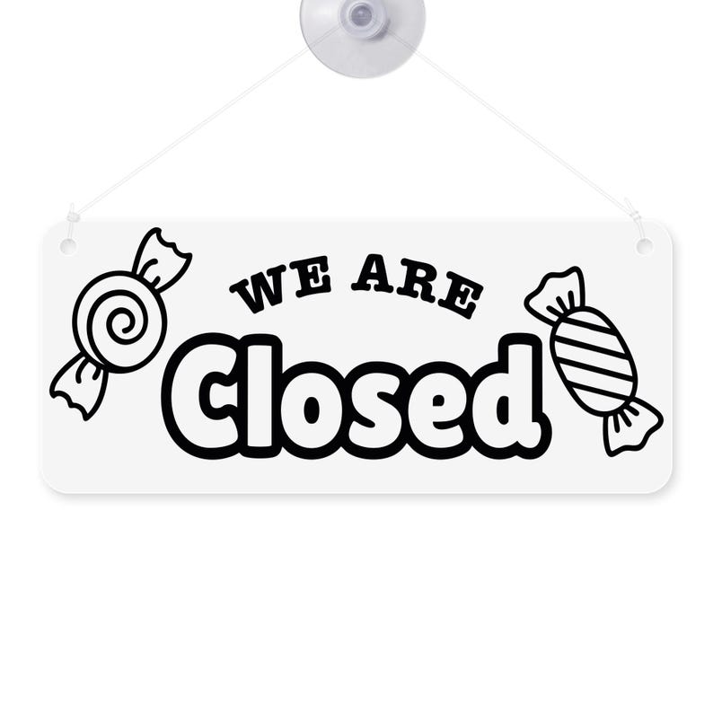 Puede incluir: Cartel rectangular blanco con las palabras "WE ARE Closed" en negro, con ilustraciones de caramelos a cada lado. El cartel est&aacute; sujeto a una ventosa transparente con una cuerda blanca.