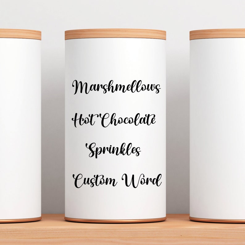 Peut inclure: Trois contenants cylindriques blancs avec des couvercles en bois. Le contenant du milieu porte une inscription en noir qui dit "Marshmallows", "Chocolat chaud", "Sprinkles" et "Mot personnalis&eacute;".