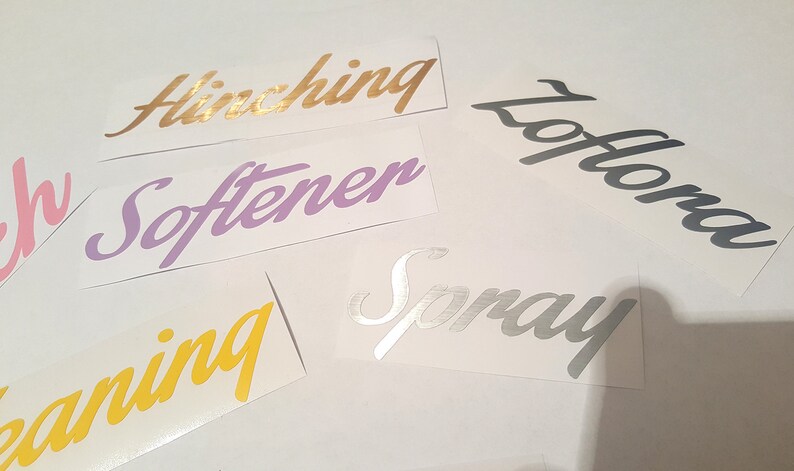 May include: Five different vinyl stickers with cursive lettering. The stickers are in various colors, including gold, purple, yellow, pink, and silver. The words on the stickers are "Hinching", "Softener", "Cleaning", "Lotion", and "Spray".