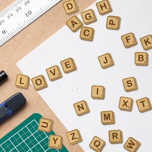 May include: A set of wooden letter tiles spelling out the word "LOVE" with other letter tiles scattered around. The tiles are brown with white lettering.