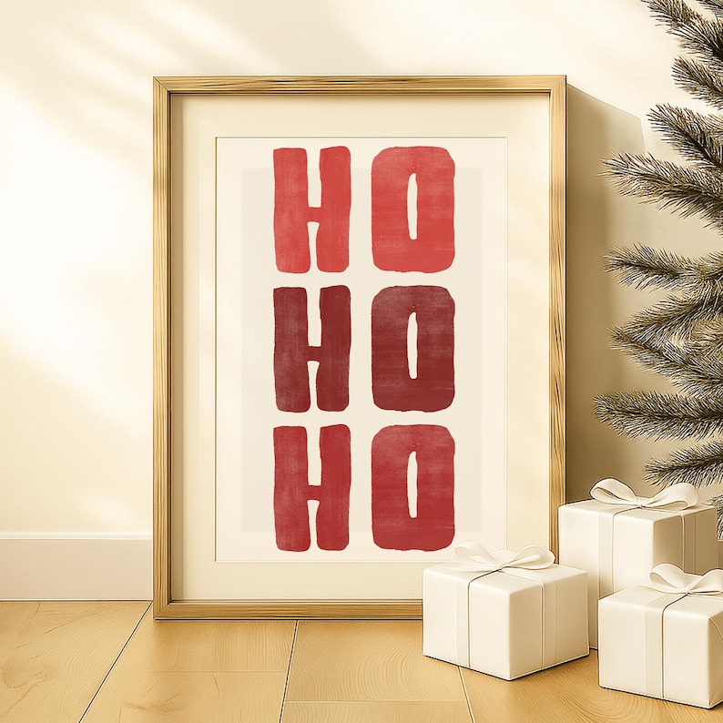 May include: Framed art print with the words "HO HO HO" in red block letters. The artwork is in a gold frame and is displayed with three wrapped white gift boxes with white ribbons. A Christmas tree is in the background.