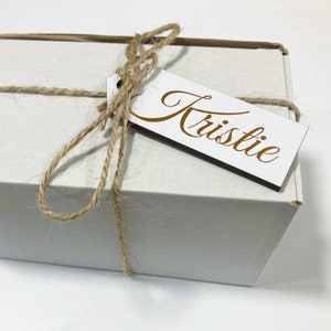 May include: A white gift box tied with twine and a wooden gift tag that says "Kristie".