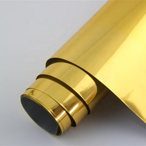 May include: A roll of gold-colored vinyl adhesive film. The film is rolled up and has a shiny, reflective surface.