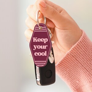 K&ouml;nnte beinhalten: Ein burgunderfarbener Schl&uuml;sselanh&auml;nger mit einem Schl&uuml;sselring aus Metall und einem Anh&auml;nger mit der Aufschrift "Keep your cool" in rosa Buchstaben.