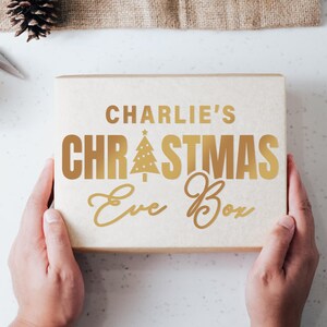 May include: A white box with gold lettering that reads "Charlie's Christmas Eve Box". The box has a gold Christmas tree design with a star on top.