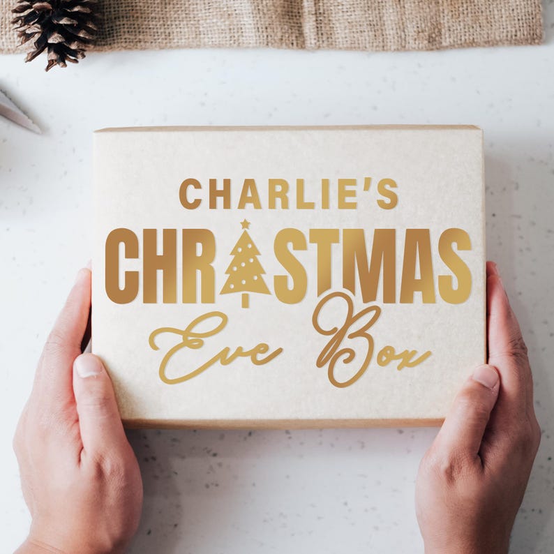 May include: A white box with gold lettering that reads "Charlie's Christmas Eve Box". The box has a gold Christmas tree design with a star on top.