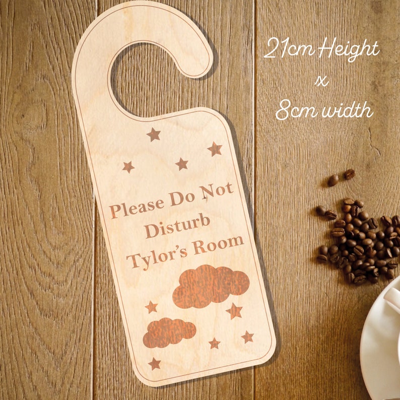 May include: Wooden door hanger with the text "Please Do Not Disturb Tyler's Room" in brown lettering. The hanger is decorated with stars and clouds. It measures 21 inches in height and 8 inches in width.