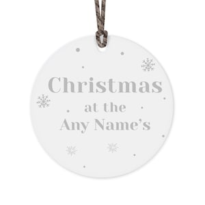 Peut inclure: Ornement de No&euml;l rond blanc avec l'inscription "Christmas at the Any Name's" en gris. L'ornement pr&eacute;sente des motifs de flocons de neige et de points, et une ficelle marron pour l'accrocher.