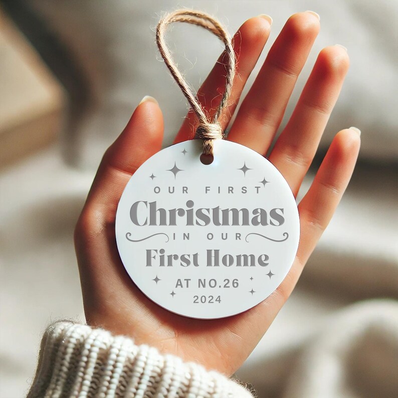 May include: White round Christmas ornament with the text "Our First Christmas in Our First Home at No. 26 2024".