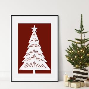 May include: A framed print featuring a white Christmas tree design on a deep red background. The tree has a star on top and is composed of horizontal lines. A small, decorated Christmas tree is to the right, with candles and gifts.