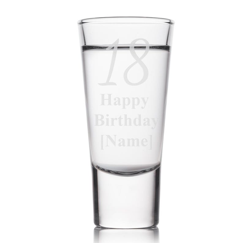 May include: A clear shot glass with the number 18 etched at the top, and the words "Happy Birthday [Name]" below. The glass is filled with a clear liquid and is set against a white background.
