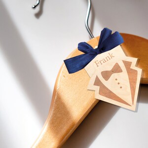 May include: A wooden hanger with a blue bow and a wooden tag that says "Frank" with a tuxedo design.