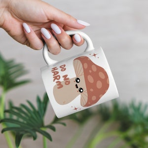 May include: White ceramic mug with a brown and red mushroom illustration. The mushroom has a smiling face and the text "Do No Harm" is written vertically on the mug.
