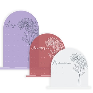 May include: Three arched acrylic signs with floral designs and names "Amy", "Anastasia", and "Monica". The signs are in shades of purple, red, and white.