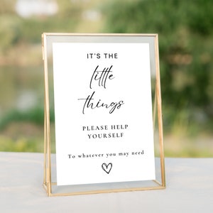 May include: A white sign with black text in a gold frame. The sign reads "It's the little things. Please help yourself to whatever you may need." with a small heart at the bottom.