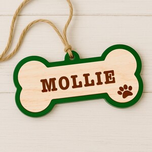 Peut inclure: Une &eacute;tiquette en forme d'os de chien en bois avec le nom "MOLLIE" en lettres marron. L'&eacute;tiquette a une bordure verte et une empreinte de patte sur le c&ocirc;t&eacute; droit. Une boucle en ficelle naturelle est attach&eacute;e pour l'accrocher.