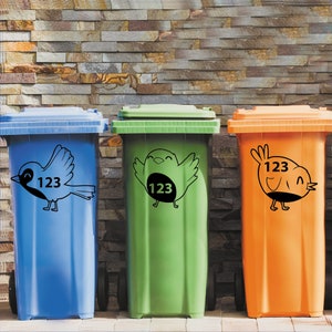 K&ouml;nnte beinhalten: Drei blaue, gr&uuml;ne und orangefarbene Recyclingbeh&auml;lter mit schwarzen Vogelaufklebern und der Nummer 123 auf jedem Beh&auml;lter.