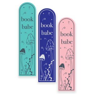 May include: Three bookmark designs with the text "book babe" and mushroom illustrations. The bookmarks are in blue, pink, and teal.