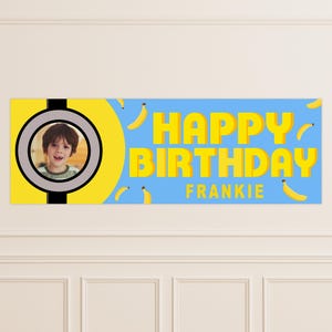 May include: A personalized birthday banner with a photo of a child in a circular frame. The banner features the text "HAPPY BIRTHDAY FRANKIE" in yellow block letters against a light blue background, with yellow banana illustrations.
