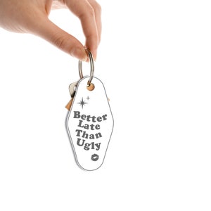 May include: White motel key chain with the text "Better Late Than Ugly" in a retro font. A small star and a lip print are also on the keychain.