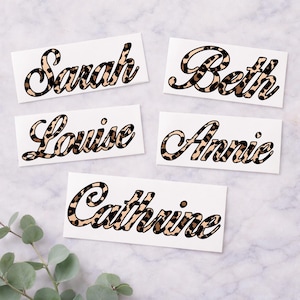 May include: Five white rectangular stickers with names in a cursive font. The names are Sarah, Beth, Louise, Annie, and Catherine. The letters are filled with a brown and tan leopard print pattern, outlined in black.