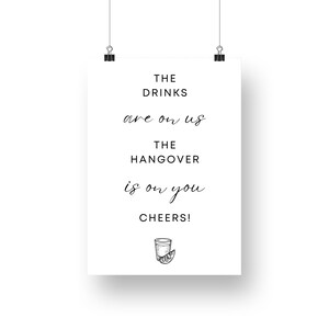 May include: A white sign with black text that reads "The drinks are on us. The hangover is on you. Cheers!" with a black and white illustration of a shot glass with a lime wedge.