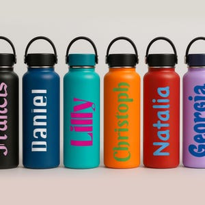 Puede incluir: Seis botellas de agua de acero inoxidable con nombres personalizados en diferentes colores. Los nombres son "Julius", "Daniel", "Lily", "Christoph", "Natalia" y "Georgia".