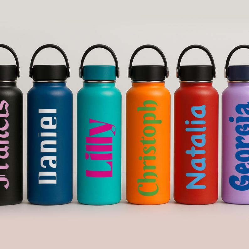 Puede incluir: Seis botellas de agua de acero inoxidable con nombres personalizados en diferentes colores. Los nombres son "Julius", "Daniel", "Lily", "Christoph", "Natalia" y "Georgia".