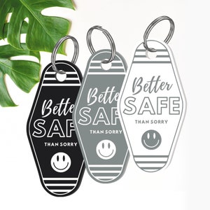 May include: Three keychains with a motel key design. Each keychain has the text "Better Safe Than Sorry" and a smiley face. The keychains are black, gray, and white.