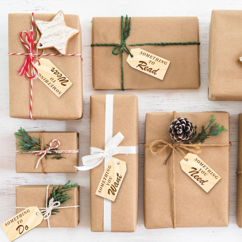 K&ouml;nnte beinhalten: Eine Sammlung von acht braunen Geschenkboxen mit Schnur und Holzetiketten. Die Etiketten tragen die Aufschrift "Something to Read", "Something to Wear", "Something to Want", "Something to Need" und "Something to Do".