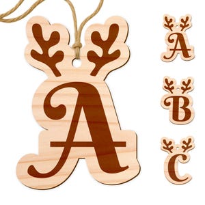 May include: Wooden Christmas ornaments in the shape of letters, with a reindeer antler design. The letter "A" is shown hanging with a twine string, and the letters "A", "B", and "C" are displayed separately. The ornaments are light brown with darker brown lettering.