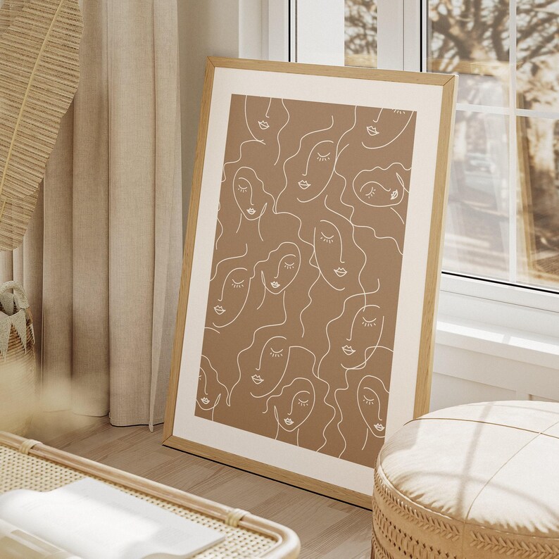 Op de afbeelding: Een ingelijst print met een minimalistisch ontwerp met meerdere abstracte gezichten in witte contouren op een bruine achtergrond.