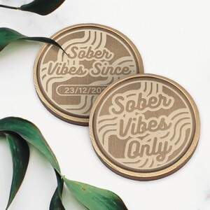 May include: Two gold-colored round coasters with a white design. The top coaster says "Sober Vibes Since" with the date "23/12/202" underneath. The bottom coaster says "Sober Vibes Only".