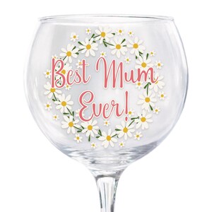 Puede incluir: Una copa de ginebra transparente con un dise&ntilde;o de corona floral de margaritas. Las palabras "Best Mum Ever!" est&aacute;n escritas en rosa dentro de la corona. Ideal para servir c&oacute;cteles u otras bebidas.