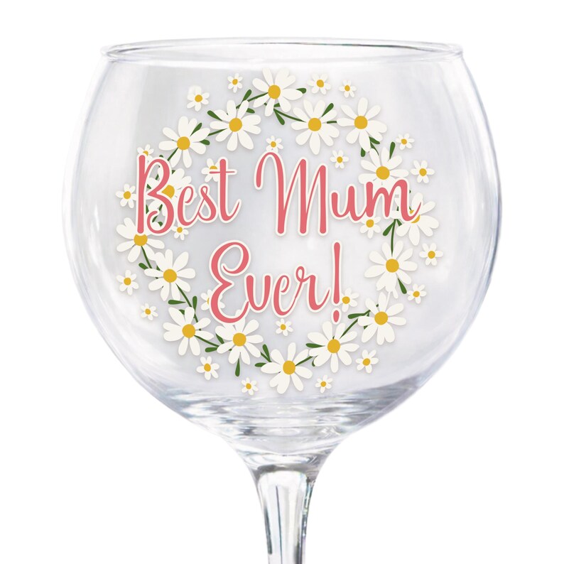 Puede incluir: Una copa de ginebra transparente con un dise&ntilde;o de corona floral de margaritas. Las palabras "Best Mum Ever!" est&aacute;n escritas en rosa dentro de la corona. Ideal para servir c&oacute;cteles u otras bebidas.