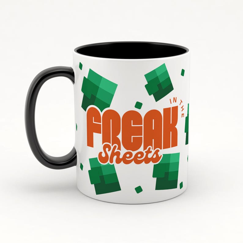 May include: White ceramic mug with a black rim and handle. The mug has a green and orange design with the text "Freak in the Sheets".