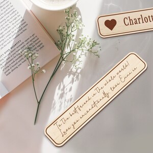 Op de afbeelding: Twee houten bladwijzers met gepersonaliseerde berichten. De eerste bladwijzer is lichtbruin met een hart en de tekst "Charlotte". De tweede bladwijzer is lichtbruin met de tekst "To the best friend in the whole world! Love you unconditionally. Love Emma xx".