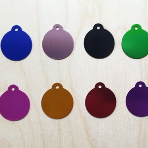 May include: Eight round metal tags in different colors: blue, purple, silver, black, green, gold, red, and purple. Each tag has a small hole at the top for attaching a ring or chain.