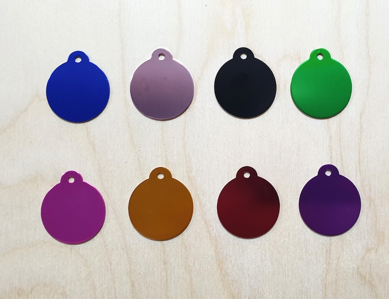 May include: Eight round metal tags in different colors: blue, purple, silver, black, green, gold, red, and purple. Each tag has a small hole at the top for attaching a ring or chain.