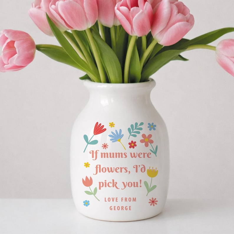 May include: A white ceramic vase with a floral design and the text "If mums were flowers, I'd pick you!" in a playful font. The vase holds a bouquet of pink tulips with green stems and leaves. "Love from George" is written at the bottom.