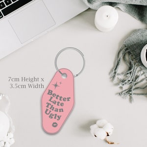 May include: Pink motel key chain with a silver key ring. The keychain is 7cm high and 3.5cm wide. The text on the keychain reads "Better Late Than Ugly".