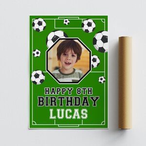 May include: A green poster with a soccer field design, soccer balls, and a photo of a child. The poster reads "HAPPY 8TH BIRTHDAY LUCAS" in bold white and black text. A rolled-up poster is visible on the right.