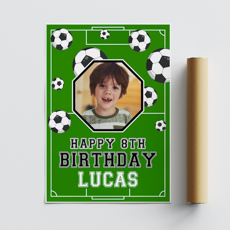 May include: A green poster with a soccer field design, soccer balls, and a photo of a child. The poster reads "HAPPY 8TH BIRTHDAY LUCAS" in bold white and black text. A rolled-up poster is visible on the right.