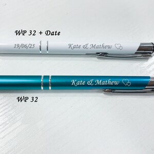 May include: Two pens with personalized engravings. The top pen is white with silver accents and the bottom pen is teal blue with silver accents. Both pens have the text "Kate & Mathew" and two hearts engraved on them. The top pen also has the text "WP 32 + Date" and "19/06/25" engraved on it. The bottom pen has the text "WP 32" engraved on it.