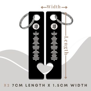 May include: Two black metal keychains with a heart-shaped cutout. Each keychain has a silver ring and a design of vertical lines and a music note symbol. The keychains measure 2.7 inches in length and 1.5 inches in width.